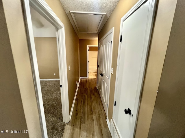 corridor with attic access, wood finished floors, a textured ceiling, and baseboards