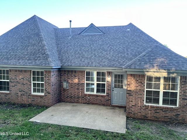 back of house with roof with shingles, a patio, and brick siding