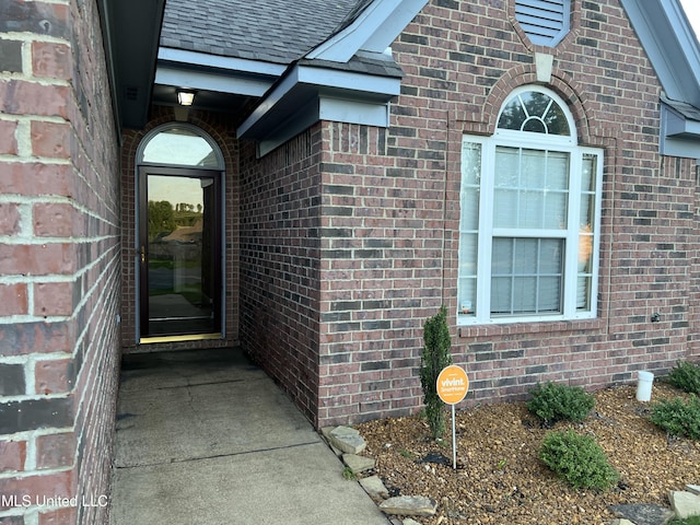 view of exterior entry featuring brick siding and a shingled roof