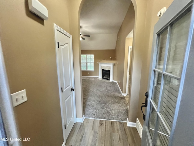 hallway featuring arched walkways, wood finished floors, and baseboards