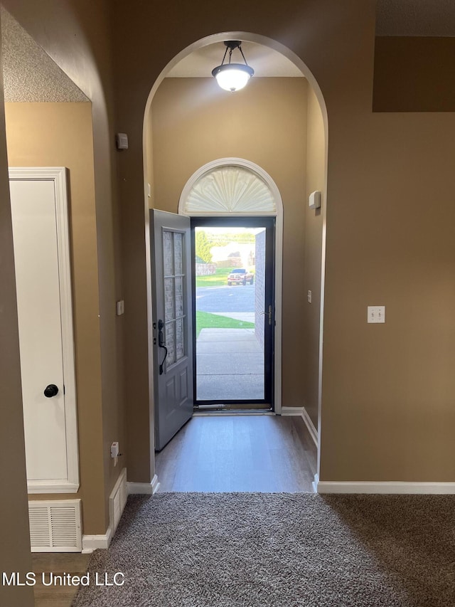 foyer with arched walkways, carpet floors, and baseboards