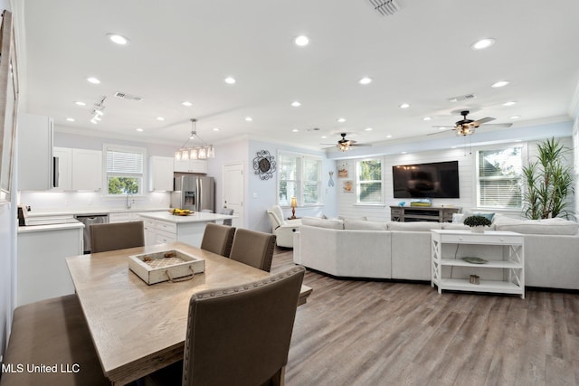 dining area with light wood-type flooring, sink, ornamental molding, and ceiling fan with notable chandelier