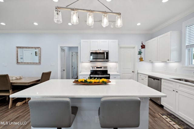 kitchen featuring appliances with stainless steel finishes, hanging light fixtures, a kitchen island, white cabinets, and dark hardwood / wood-style flooring