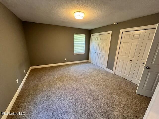 unfurnished bedroom featuring dark carpet, a textured ceiling, and two closets