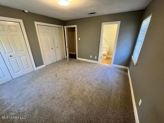 unfurnished bedroom featuring multiple closets, ensuite bath, carpet flooring, and a textured ceiling