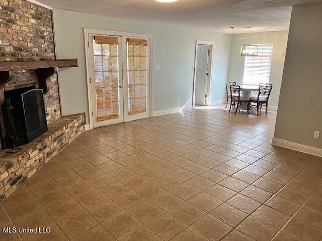 unfurnished living room with a fireplace, tile patterned floors, french doors, and a textured ceiling