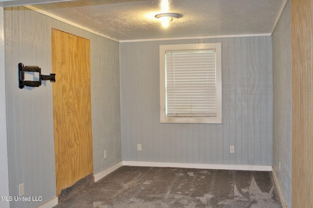 unfurnished room featuring dark carpet, ornamental molding, wooden walls, and a textured ceiling