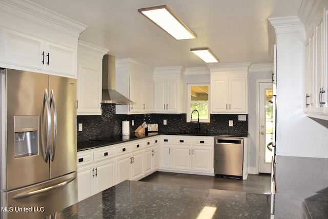 kitchen with wall chimney range hood, appliances with stainless steel finishes, white cabinetry, ornamental molding, and sink