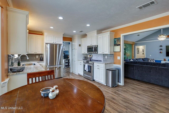 kitchen featuring sink, light hardwood / wood-style flooring, appliances with stainless steel finishes, ornamental molding, and white cabinets