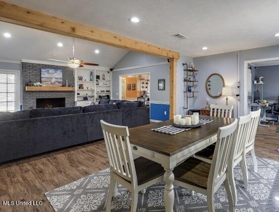 dining area featuring hardwood / wood-style flooring, ceiling fan, a fireplace, and lofted ceiling with beams