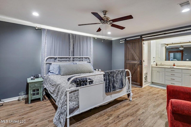 bedroom with ensuite bath, ornamental molding, a barn door, and light hardwood / wood-style flooring