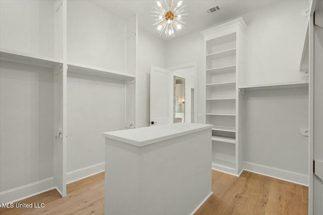 spacious closet featuring light wood-type flooring, visible vents, and an inviting chandelier