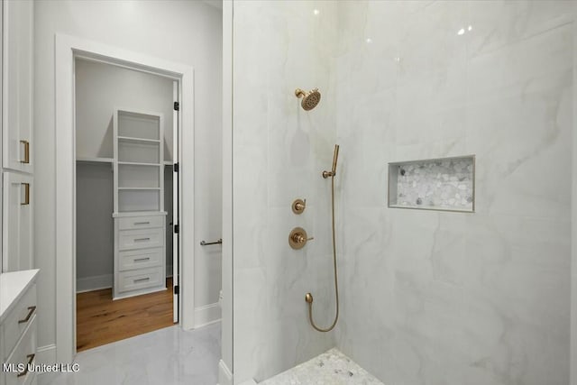 bathroom featuring a spacious closet, a marble finish shower, and vanity