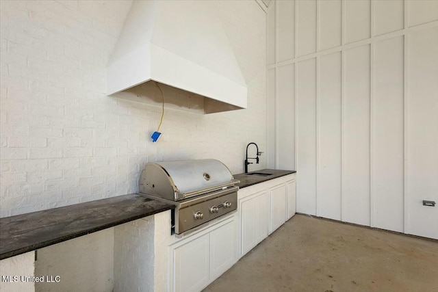 kitchen featuring dark countertops, brick wall, premium range hood, concrete floors, and a sink