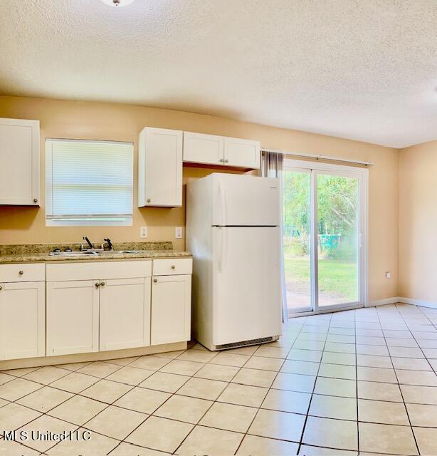 2614 George St, Gulfport, MS 39503 - kitchen with freestanding refrigerator, a textured ceiling, a sink, white cabinetry, and light tile patterned floors