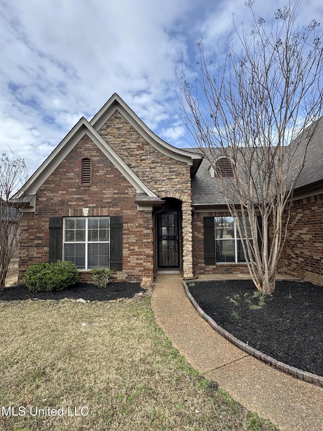 single story home with a front yard, brick siding, stone siding, and a shingled roof