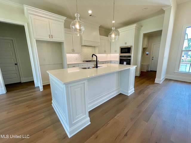 kitchen with dark wood-type flooring, a center island with sink, pendant lighting, white cabinetry, and appliances with stainless steel finishes