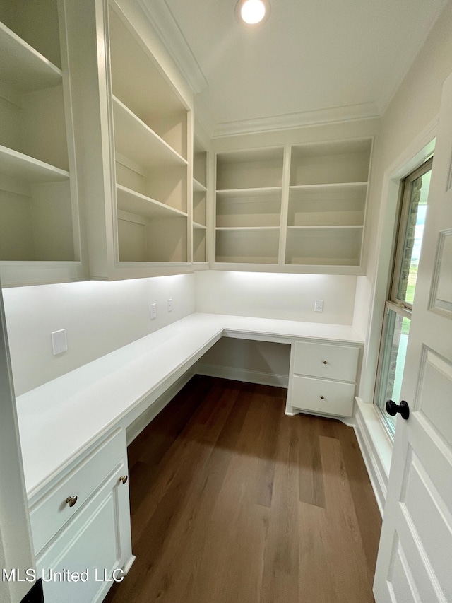 unfurnished office with built in desk, crown molding, and hardwood / wood-style floors