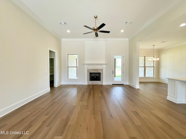 unfurnished living room featuring ceiling fan with notable chandelier, ornamental molding, wood-type flooring, and a fireplace