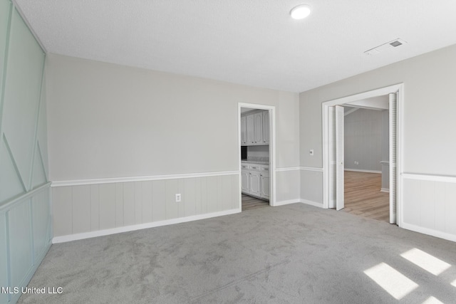 unfurnished bedroom with visible vents, carpet, and a wainscoted wall