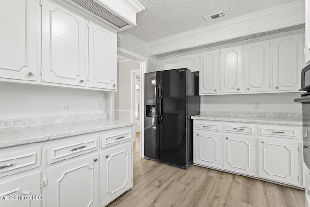 kitchen with visible vents, light wood-style flooring, black fridge, and white cabinetry