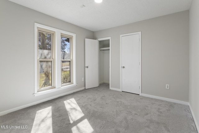 unfurnished bedroom with two closets, baseboards, a textured ceiling, and carpet flooring