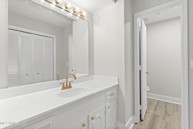 bathroom featuring baseboards, toilet, wood finished floors, and vanity