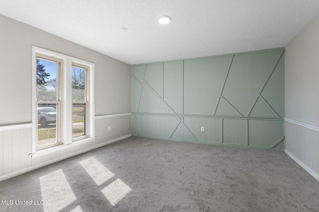 carpeted empty room with plenty of natural light, a textured ceiling, and a decorative wall