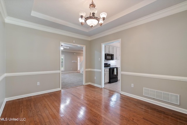 spare room with a notable chandelier, ornamental molding, a tray ceiling, and light wood-type flooring