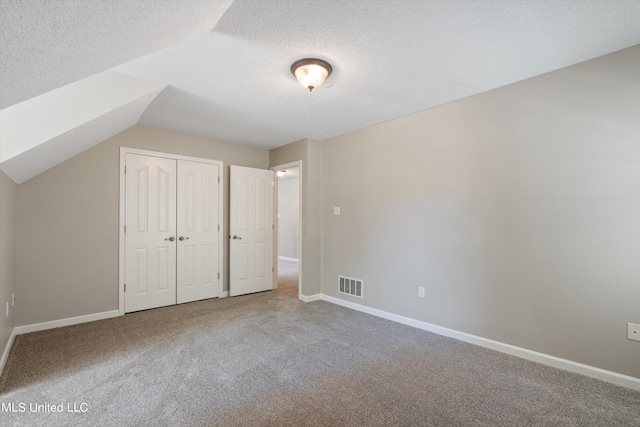 unfurnished bedroom with lofted ceiling, a textured ceiling, a closet, and carpet floors