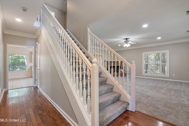 staircase featuring ceiling fan, hardwood / wood-style flooring, ornamental molding, and plenty of natural light