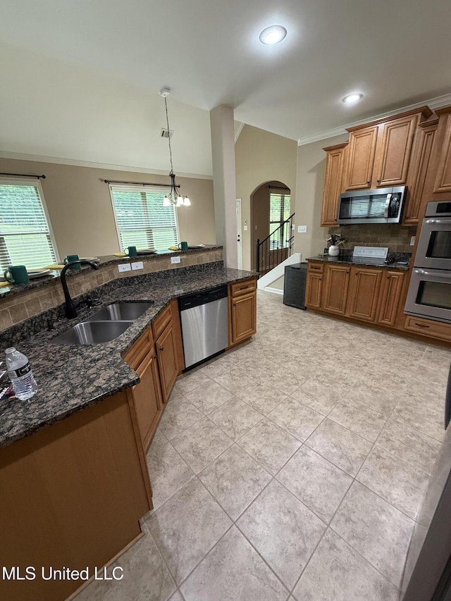 7419 Rose Garden Ln, Olive Branch, MS 38654 - kitchen with stainless steel appliances, a sink, arched walkways, brown cabinetry, and dark stone counters