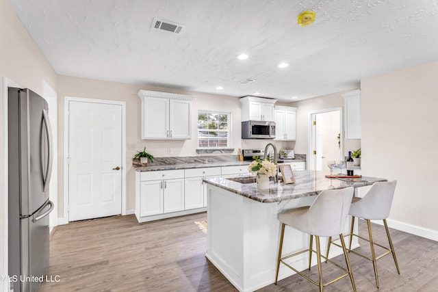 kitchen with white cabinetry, stainless steel appliances, a breakfast bar area, and stone counters