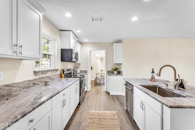 kitchen with appliances with stainless steel finishes, light stone countertops, sink, and white cabinets