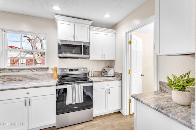 kitchen with white cabinetry, light stone countertops, light hardwood / wood-style floors, and appliances with stainless steel finishes