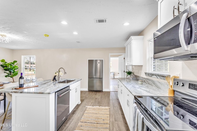 kitchen featuring sink, white cabinetry, light stone counters, appliances with stainless steel finishes, and a kitchen island with sink