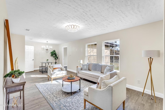 living room with an inviting chandelier, light hardwood / wood-style floors, and a textured ceiling