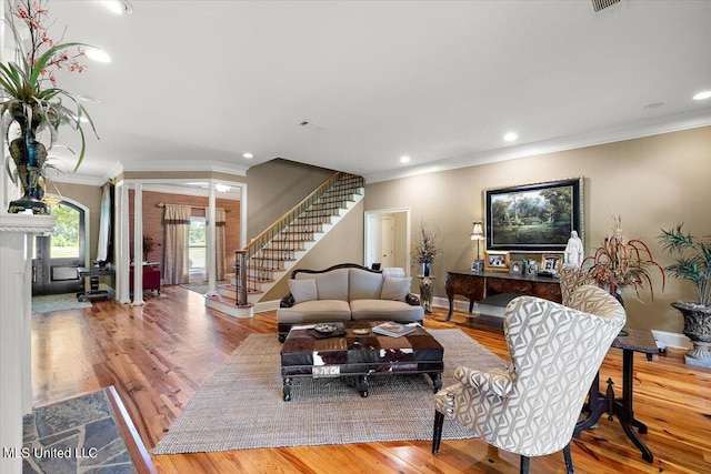 living room with crown molding, ornate columns, and light wood-type flooring