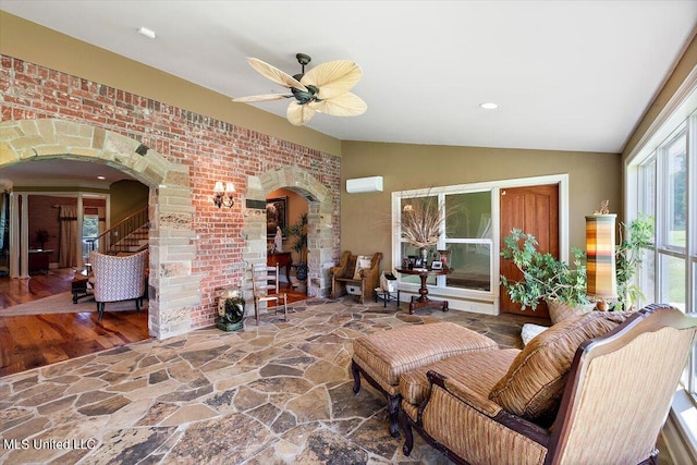 living room featuring lofted ceiling, ceiling fan, wood-type flooring, and brick wall