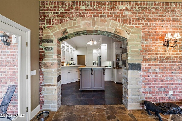 kitchen featuring a kitchen island, brick wall, ornamental molding, pendant lighting, and white cabinets