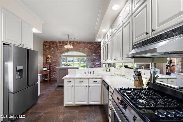 kitchen with white cabinets, appliances with stainless steel finishes, pendant lighting, sink, and brick wall