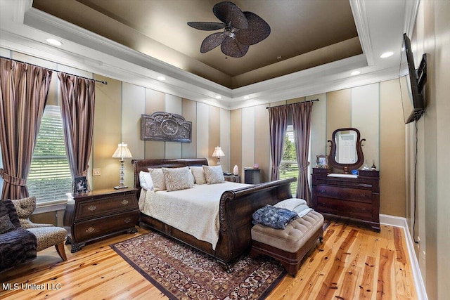 bedroom with light hardwood / wood-style floors, ceiling fan, and a raised ceiling