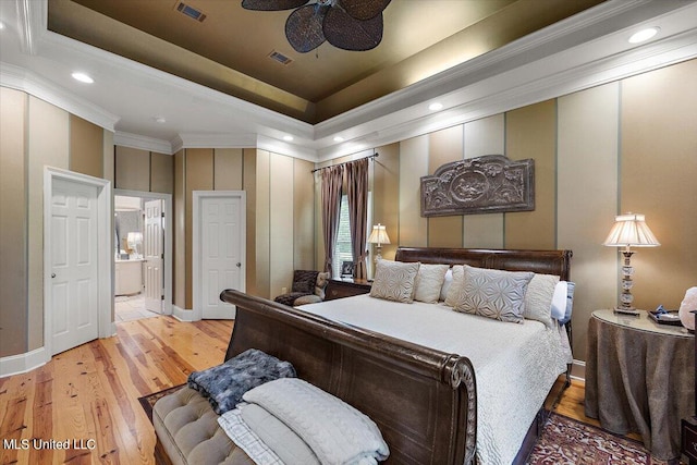 bedroom featuring ceiling fan, a tray ceiling, ensuite bathroom, light hardwood / wood-style floors, and crown molding