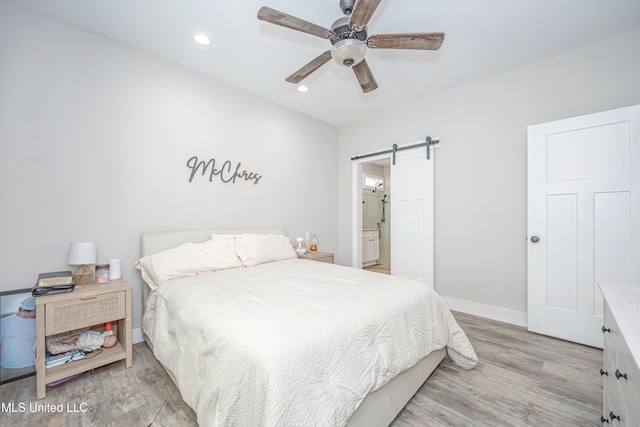 bedroom featuring ceiling fan, connected bathroom, a barn door, and light hardwood / wood-style floors