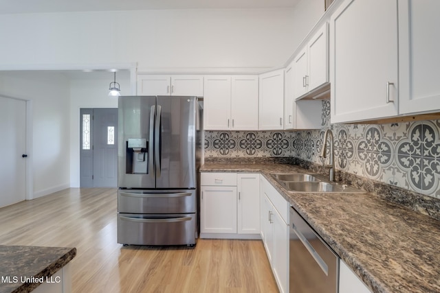 kitchen with light wood-style flooring, a sink, stainless steel appliances, white cabinetry, and backsplash