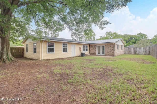 ranch-style house featuring central air condition unit, french doors, a fenced backyard, metal roof, and a front lawn
