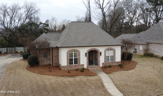 view of front of home featuring stucco siding, roof with shingles, fence, and brick siding