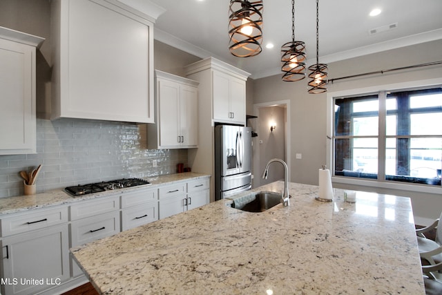 kitchen featuring appliances with stainless steel finishes, sink, decorative light fixtures, white cabinets, and a center island with sink