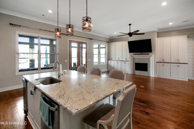 kitchen featuring a center island with sink, light stone counters, white cabinetry, pendant lighting, and sink