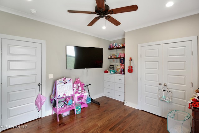 playroom featuring dark wood-type flooring, crown molding, and ceiling fan